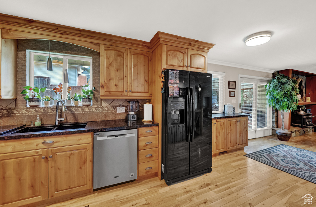 Kitchen with tasteful backsplash, light hardwood / wood-style floors, black fridge, and stainless steel dishwasher