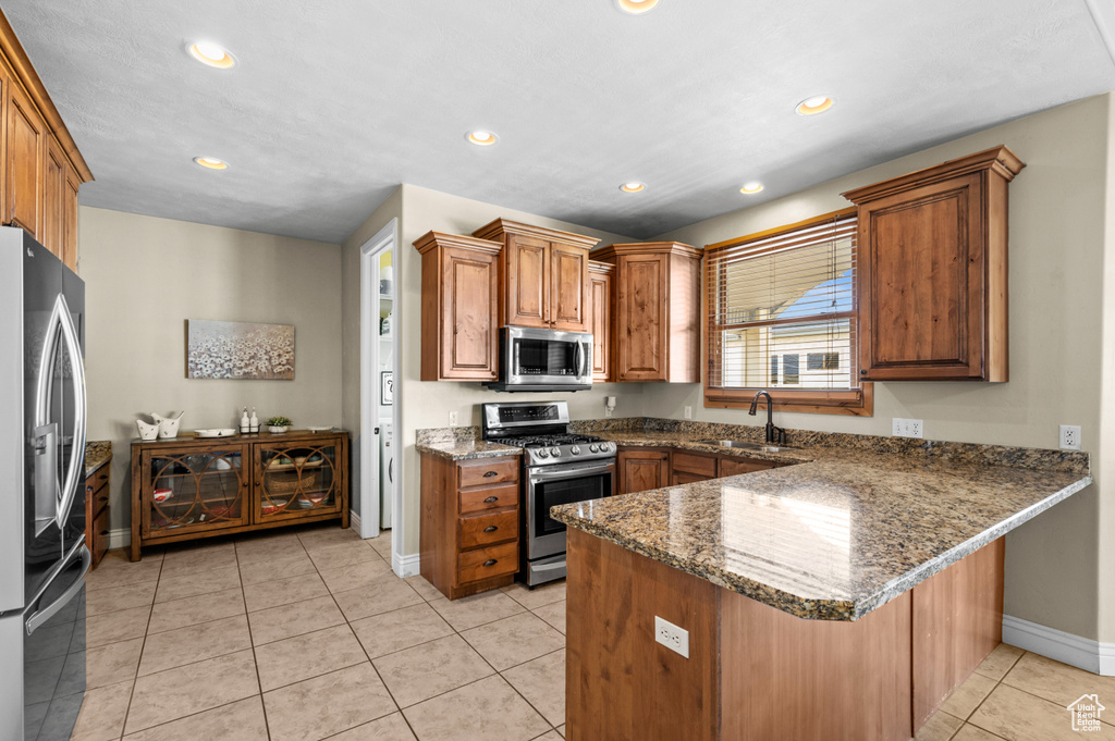 Kitchen featuring a breakfast bar, light tile flooring, kitchen peninsula, appliances with stainless steel finishes, and sink