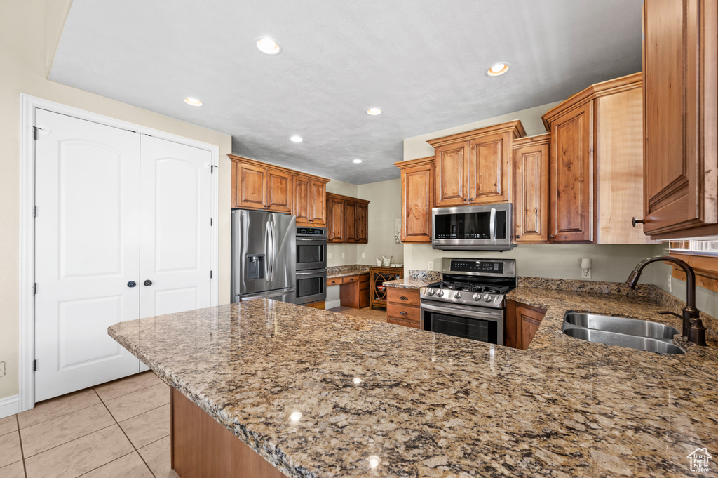Kitchen featuring sink, appliances with stainless steel finishes, light tile flooring, and light stone countertops