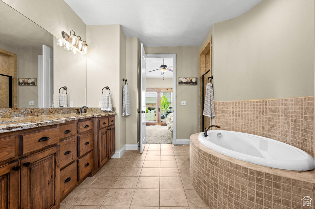Bathroom featuring ceiling fan, tile floors, dual vanity, and tiled tub