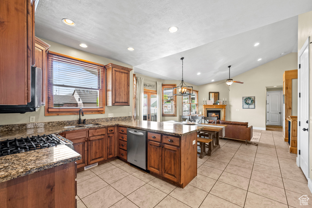 Kitchen featuring dishwasher, lofted ceiling, kitchen peninsula, dark stone countertops, and pendant lighting