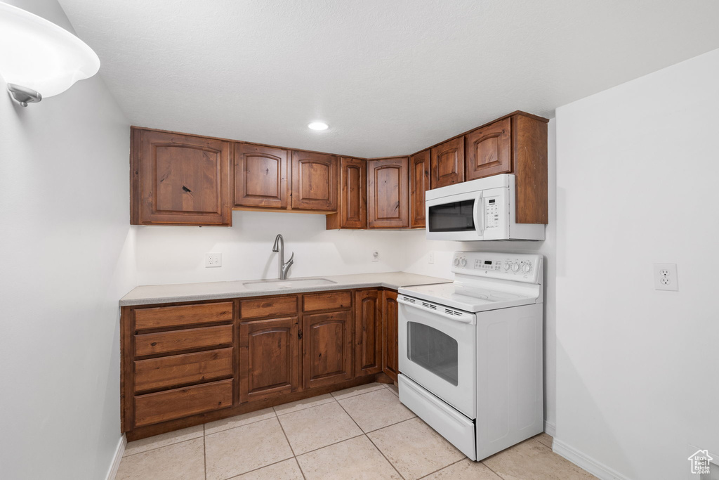 Kitchen with sink, white appliances, and light tile flooring