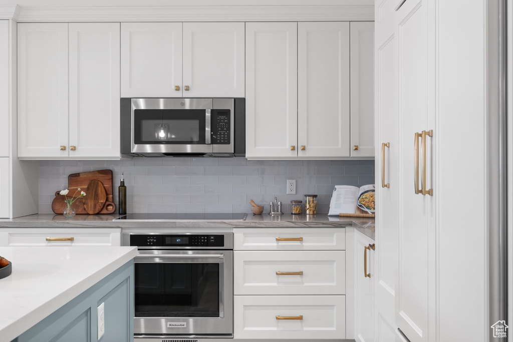 Kitchen featuring tasteful backsplash, white cabinetry, and stainless steel appliances