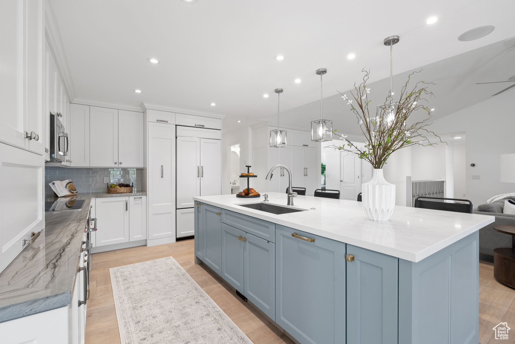 Kitchen with decorative light fixtures, a large island with sink, white cabinets, and tasteful backsplash