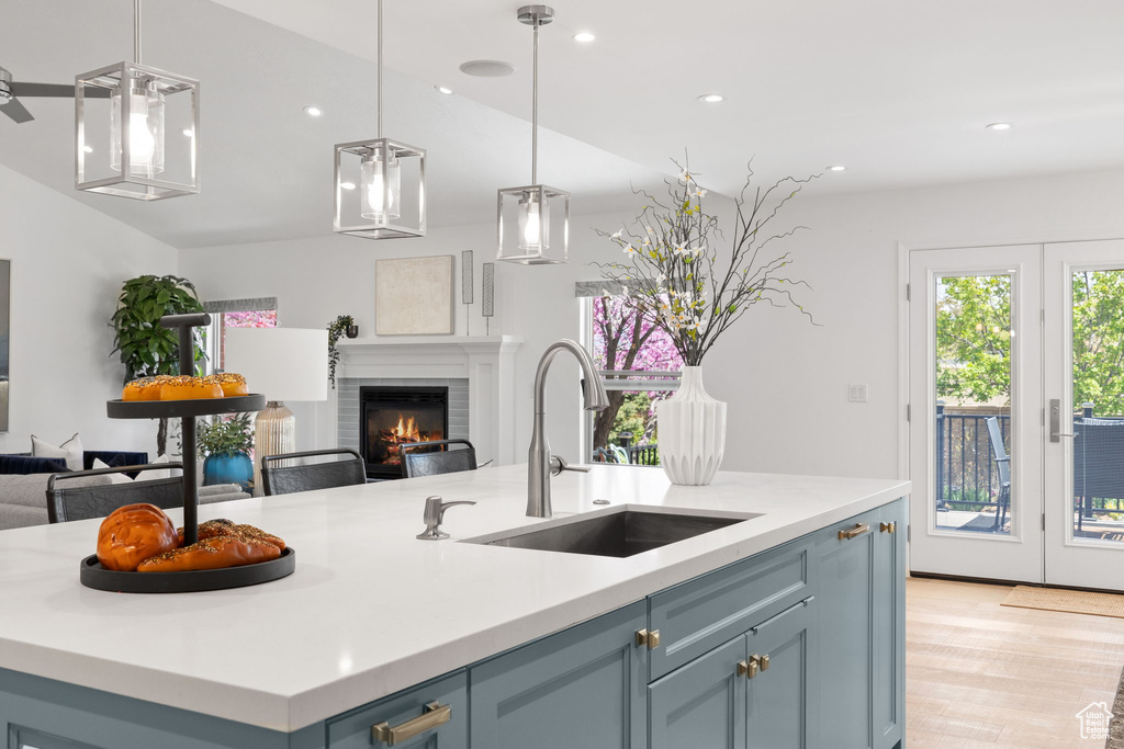 Kitchen featuring pendant lighting, light hardwood / wood-style flooring, an island with sink, sink, and blue cabinets