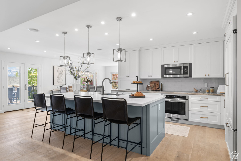 Kitchen with appliances with stainless steel finishes, light hardwood / wood-style flooring, sink, white cabinetry, and a center island with sink