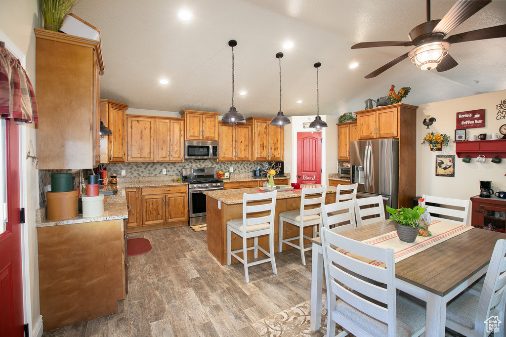 Kitchen featuring appliances with stainless steel finishes, backsplash, a kitchen island, ceiling fan, and hardwood / wood-style flooring