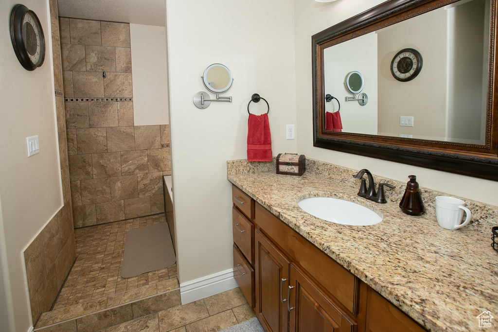 Bathroom with tiled shower, vanity with extensive cabinet space, and tile flooring