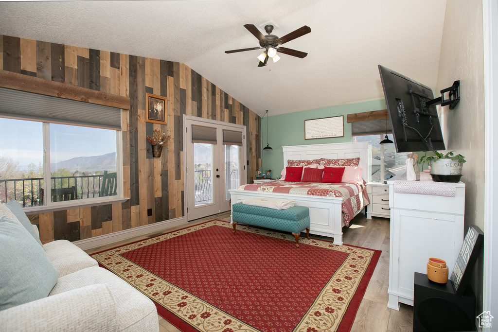 Bedroom with ceiling fan, light hardwood / wood-style floors, lofted ceiling, wooden walls, and access to outside