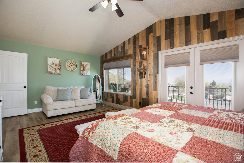 Bedroom featuring ceiling fan, access to exterior, dark wood-type flooring, wooden walls, and vaulted ceiling