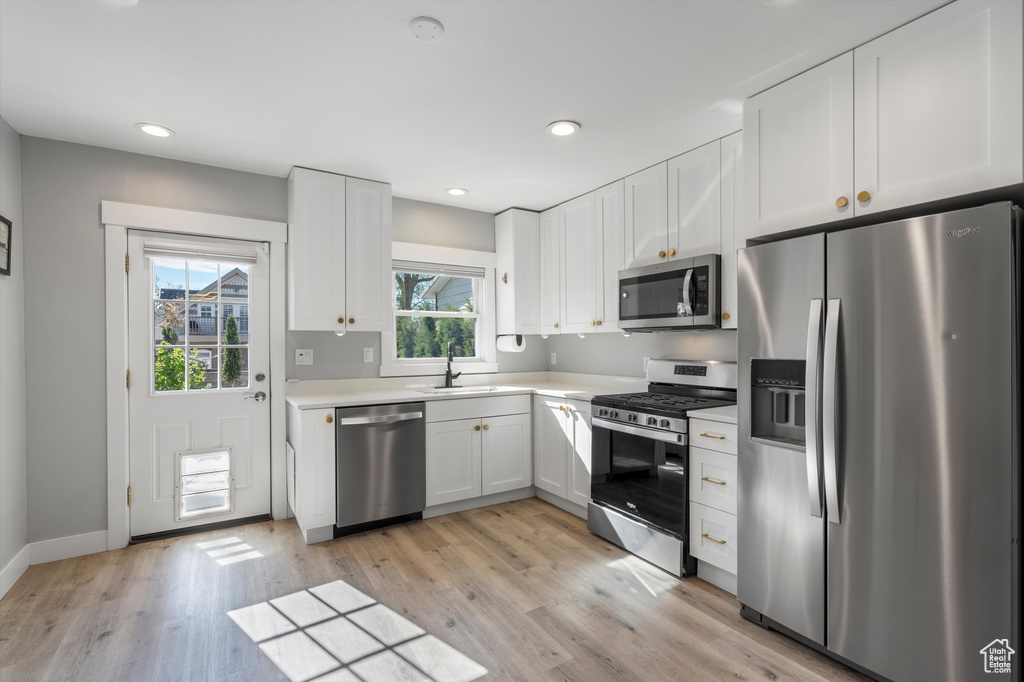 Kitchen with appliances with stainless steel finishes, sink, light hardwood / wood-style floors, and white cabinetry