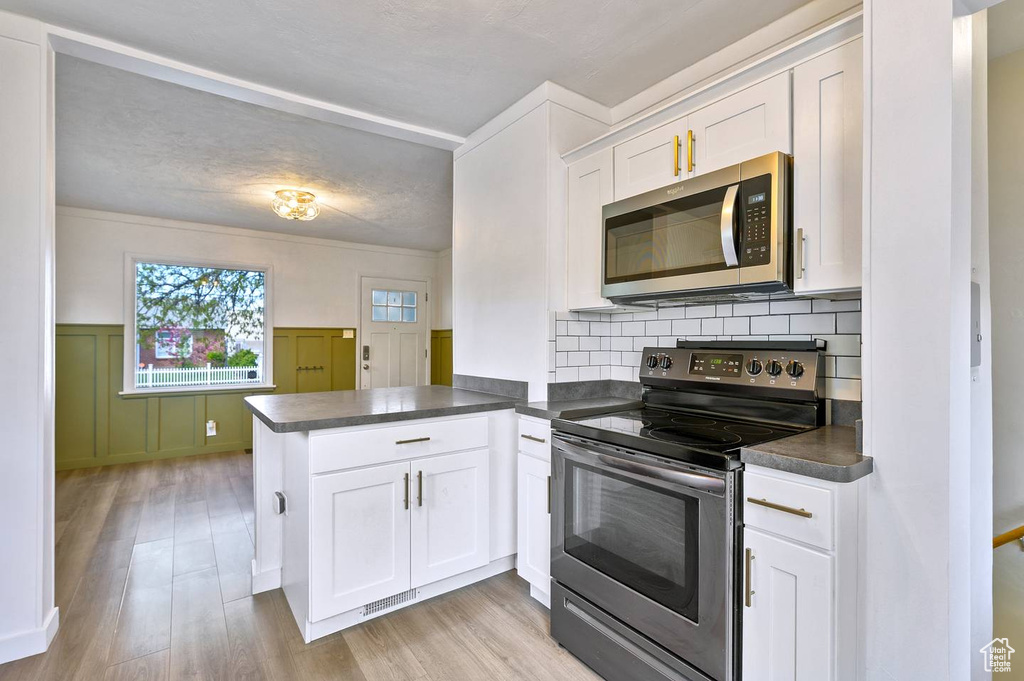 Kitchen with kitchen peninsula, backsplash, light hardwood / wood-style flooring, stainless steel appliances, and white cabinetry