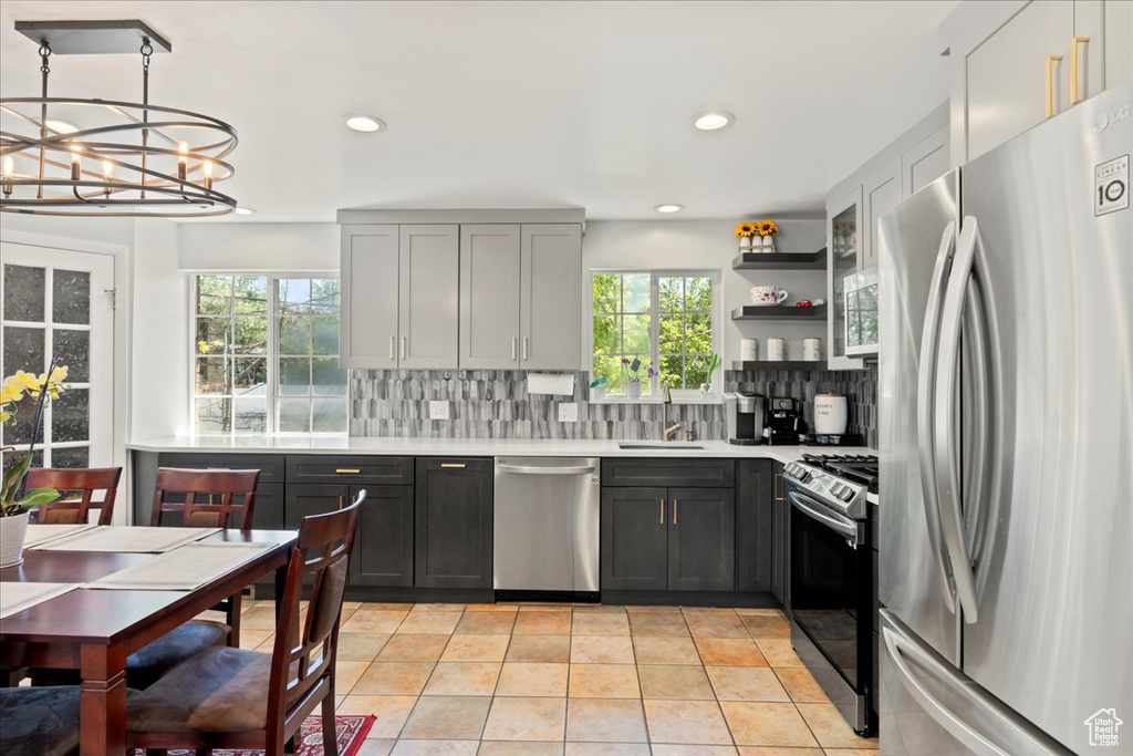 Kitchen featuring appliances with stainless steel finishes, backsplash, hanging light fixtures, a chandelier, and light tile floors