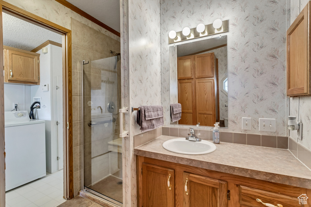 Bathroom featuring large vanity, a textured ceiling, an enclosed shower, washer / clothes dryer, and ornamental molding