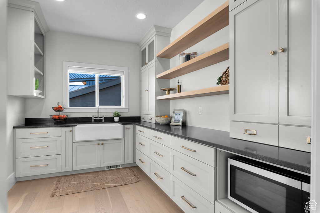 Kitchen featuring light hardwood / wood-style floors, stainless steel microwave, white cabinets, and sink
