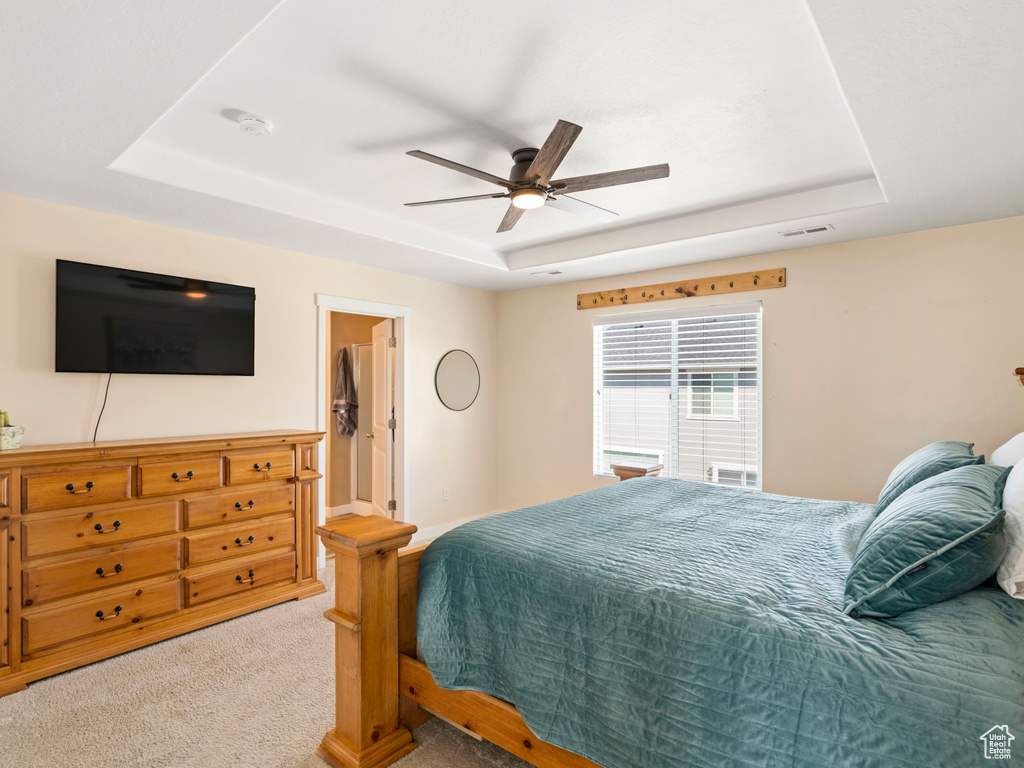 Bedroom featuring light carpet, ceiling fan, and a raised ceiling