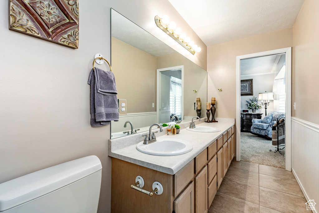 Bathroom with tile floors, vanity with extensive cabinet space, toilet, and double sink