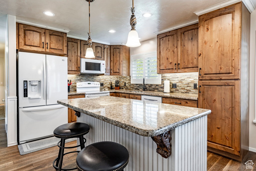 Kitchen with a center island, pendant lighting, white appliances, dark hardwood / wood-style flooring, and tasteful backsplash