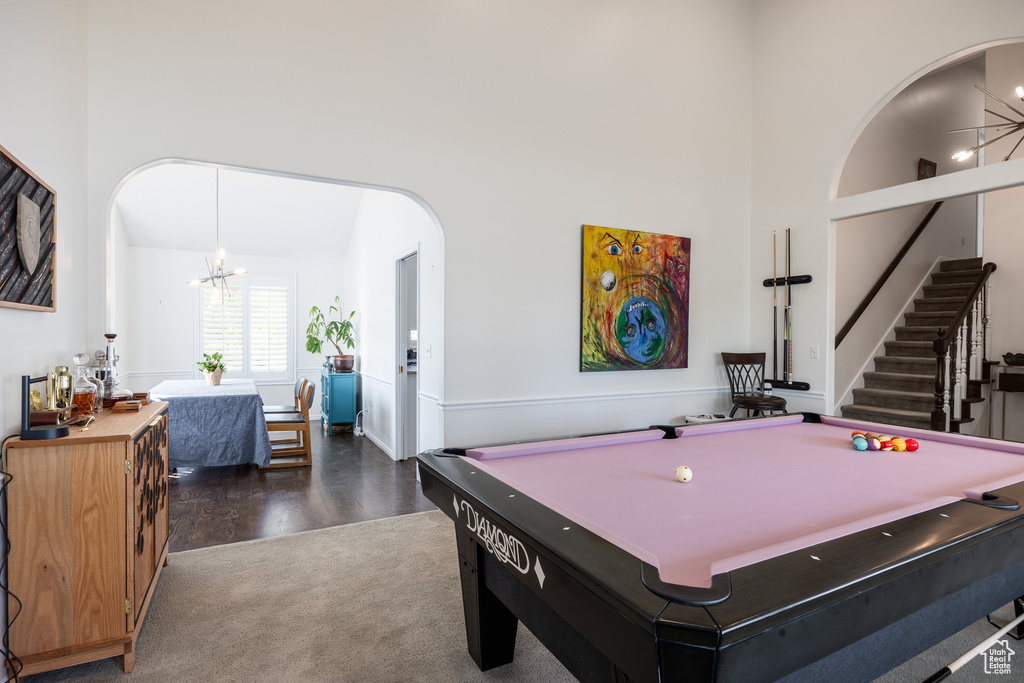 Rec room featuring dark hardwood / wood-style floors, pool table, a towering ceiling, and a notable chandelier
