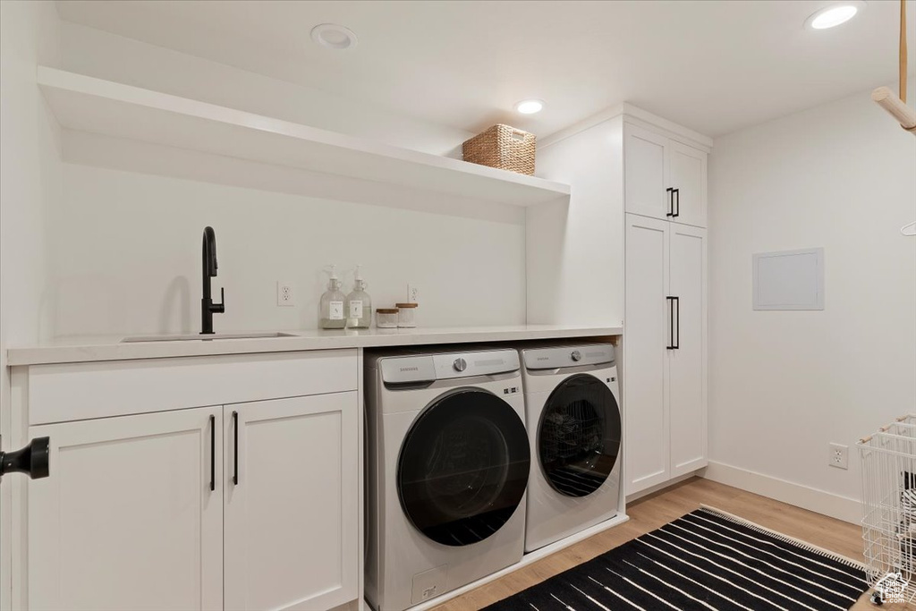 Laundry room with light hardwood / wood-style flooring, sink, separate washer and dryer, and cabinets
