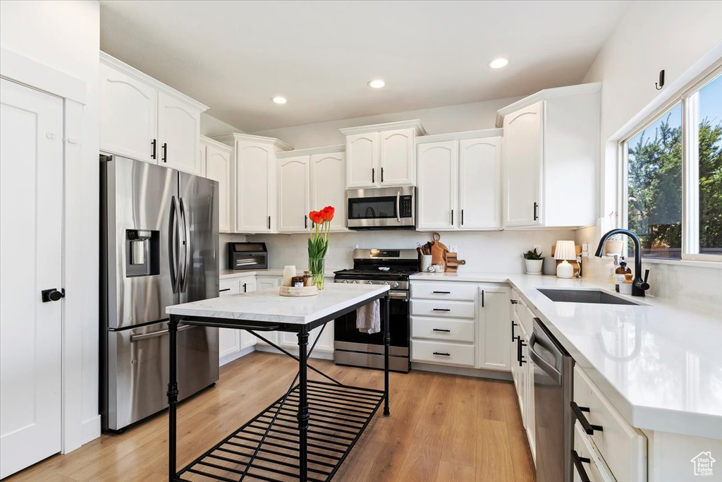 Kitchen featuring white cabinets, sink, stainless steel appliances, and light wood-type flooring