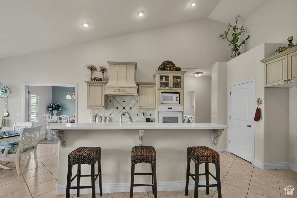 Kitchen with cream cabinets, white appliances, premium range hood, and light tile floors