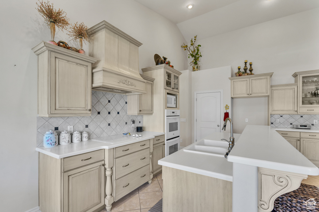 Kitchen featuring premium range hood, tasteful backsplash, a kitchen island with sink, sink, and light tile floors