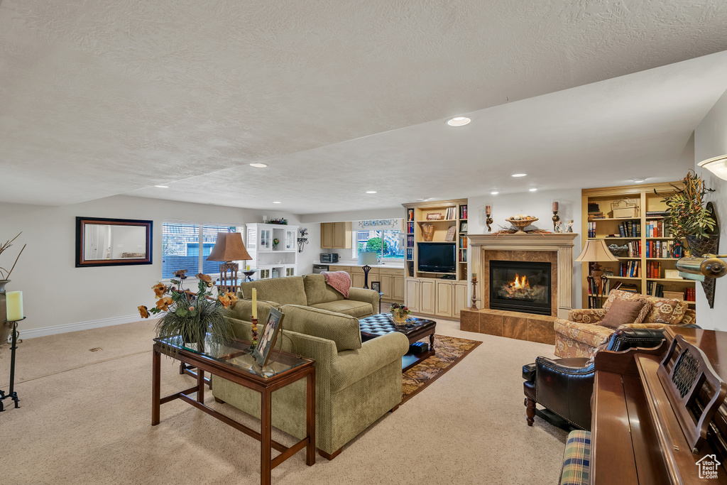 Carpeted living room featuring a tile fireplace, built in shelves, and a textured ceiling