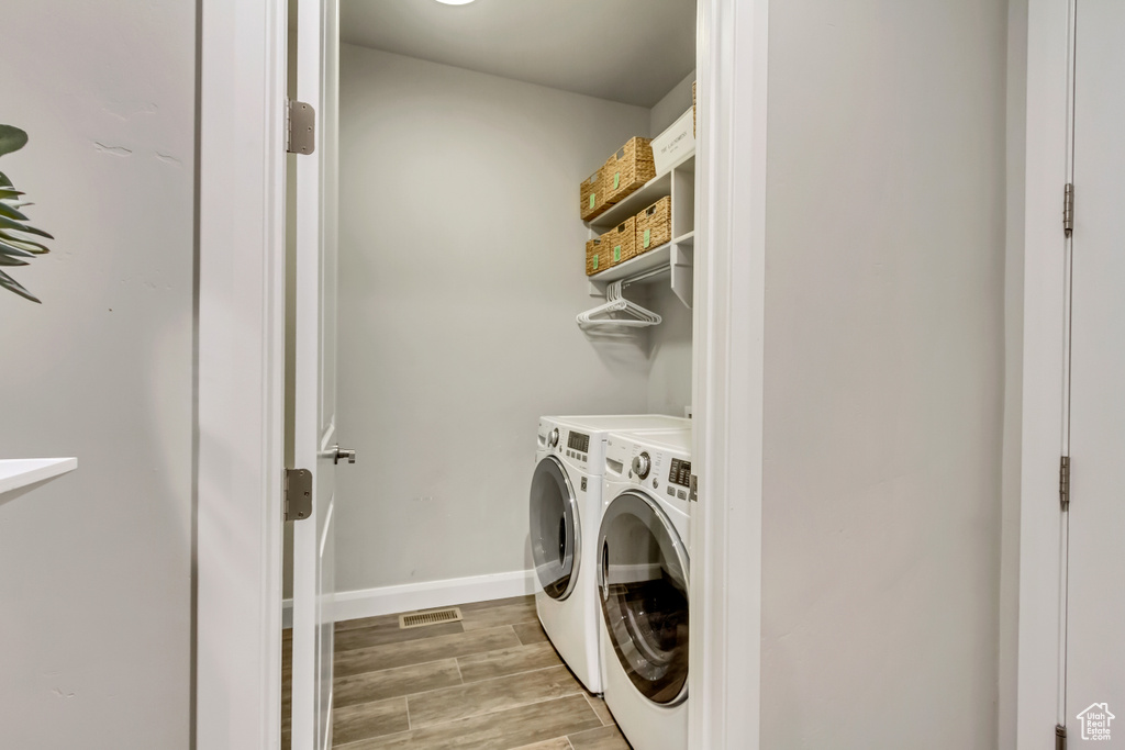 Clothes washing area with light hardwood / wood-style floors and washing machine and dryer