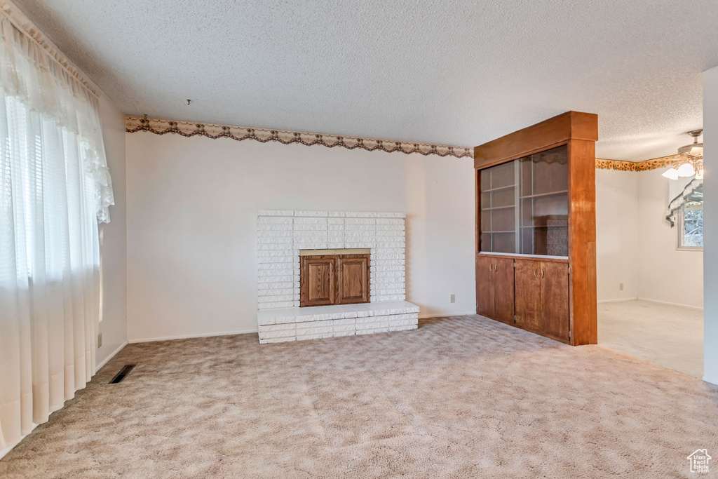 Unfurnished living room with plenty of natural light, light carpet, a textured ceiling, and a brick fireplace