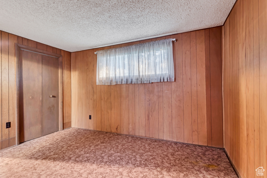 Carpeted spare room with wood walls and a textured ceiling