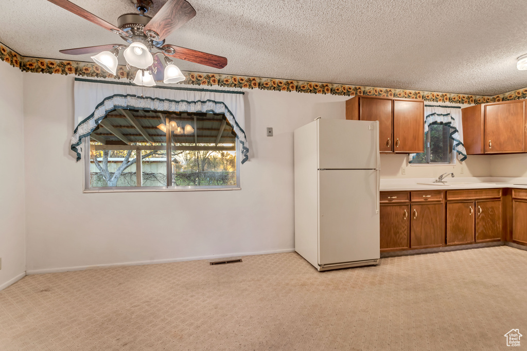Kitchen featuring white refrigerator, light colored carpet, ceiling fan, and a textured ceiling