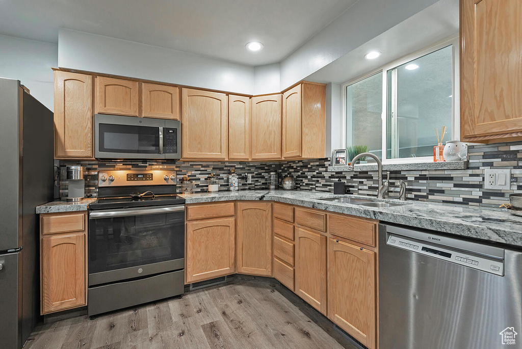 Kitchen featuring light brown cabinets, stainless steel appliances, sink, hardwood / wood-style flooring, and tasteful backsplash