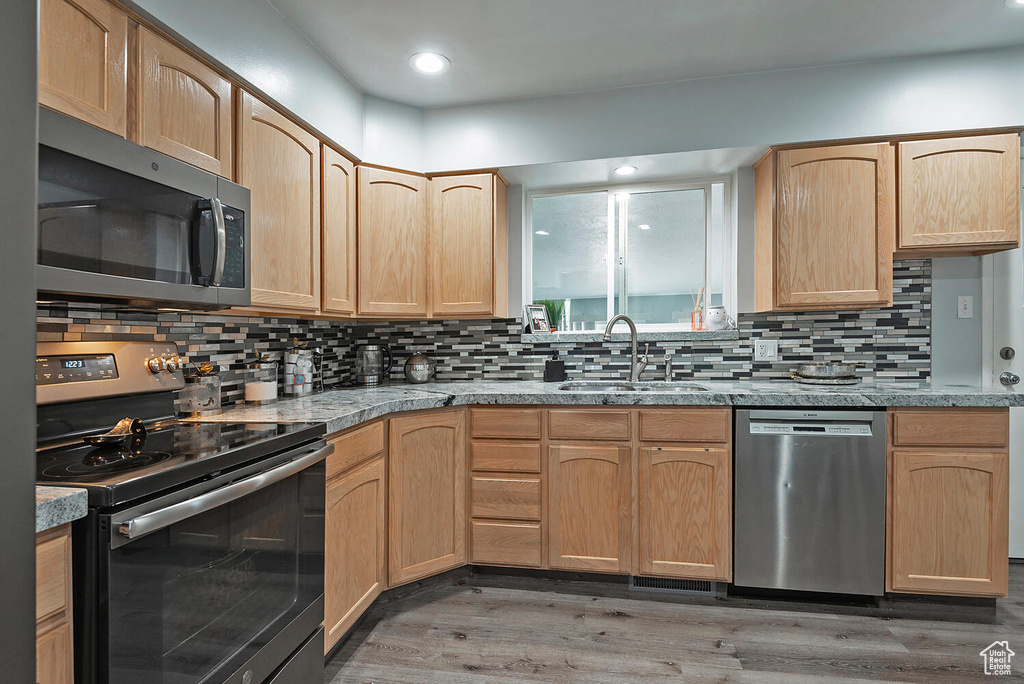 Kitchen with hardwood / wood-style floors, sink, appliances with stainless steel finishes, and tasteful backsplash