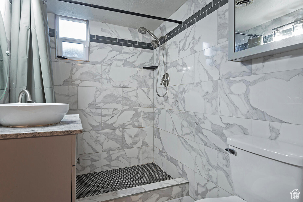 Bathroom featuring vanity with extensive cabinet space, tile walls, toilet, and a shower with shower curtain