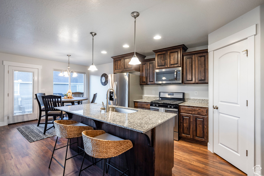 Kitchen with decorative light fixtures, appliances with stainless steel finishes, a center island with sink, dark hardwood / wood-style floors, and a chandelier