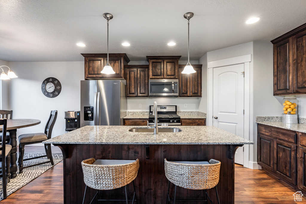 Kitchen featuring hanging light fixtures, stainless steel appliances, dark hardwood / wood-style flooring, and an island with sink