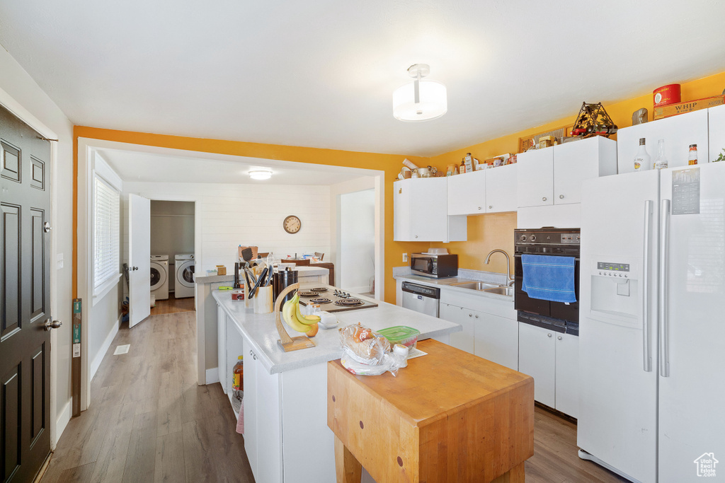 Kitchen with appliances with stainless steel finishes, white cabinets, sink, hardwood / wood-style floors, and independent washer and dryer