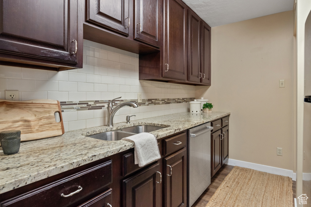 Kitchen with light stone counters, sink, dishwasher, backsplash, and dark brown cabinets