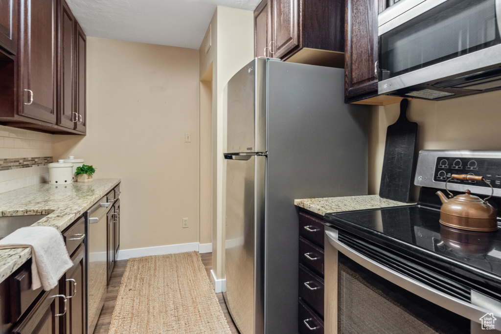 Kitchen featuring wood-type flooring, light stone countertops, dark brown cabinets, stainless steel appliances, and tasteful backsplash
