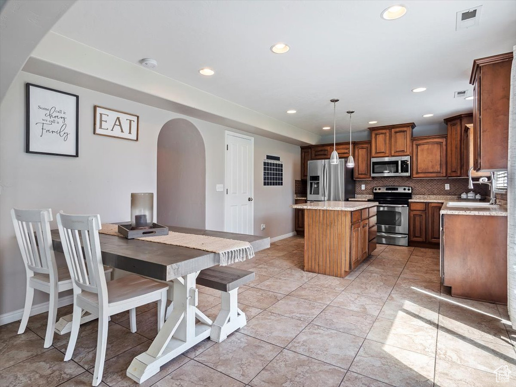 Kitchen with appliances with stainless steel finishes, a kitchen island, sink, backsplash, and light tile flooring