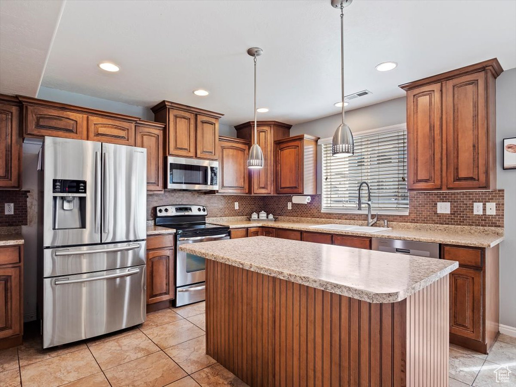 Kitchen featuring appliances with stainless steel finishes, a center island, light tile flooring, tasteful backsplash, and pendant lighting