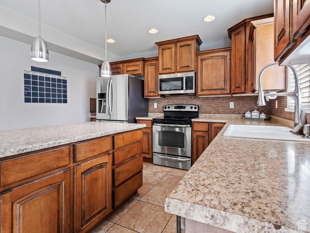 Kitchen featuring appliances with stainless steel finishes, backsplash, hanging light fixtures, sink, and light tile floors
