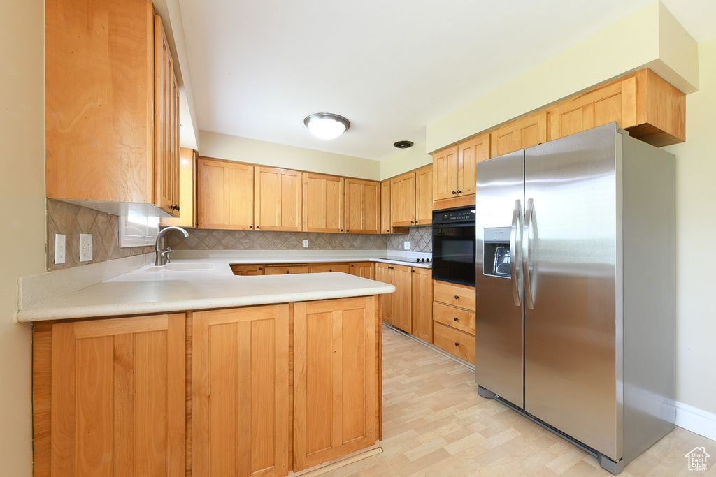 Kitchen with kitchen peninsula, stainless steel fridge with ice dispenser, backsplash, oven, and sink