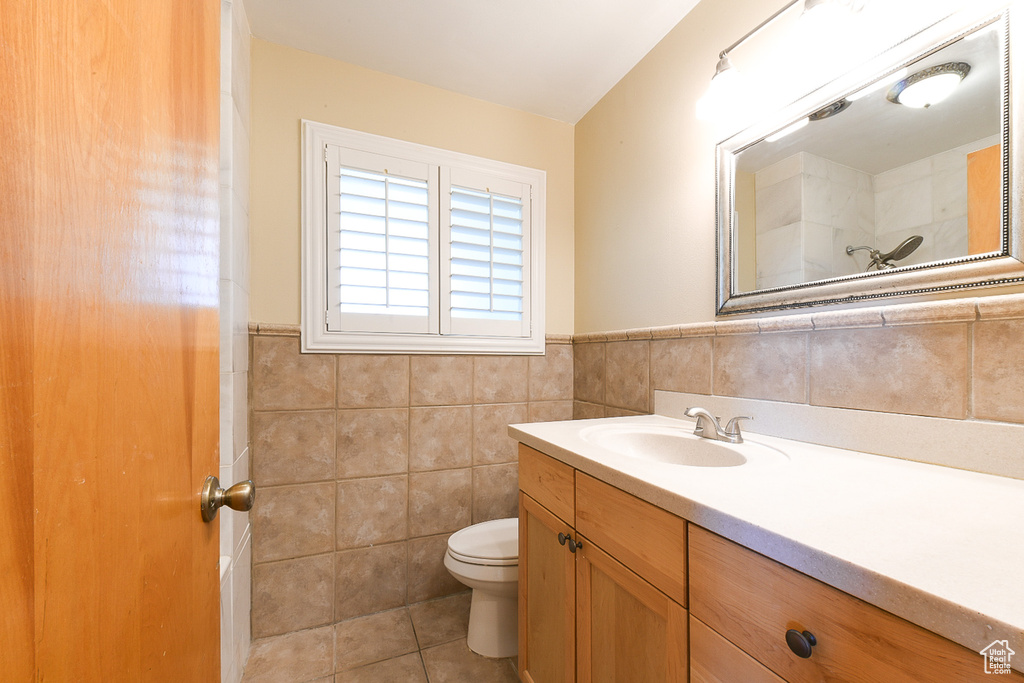 Bathroom with tile flooring, tile walls, toilet, and large vanity