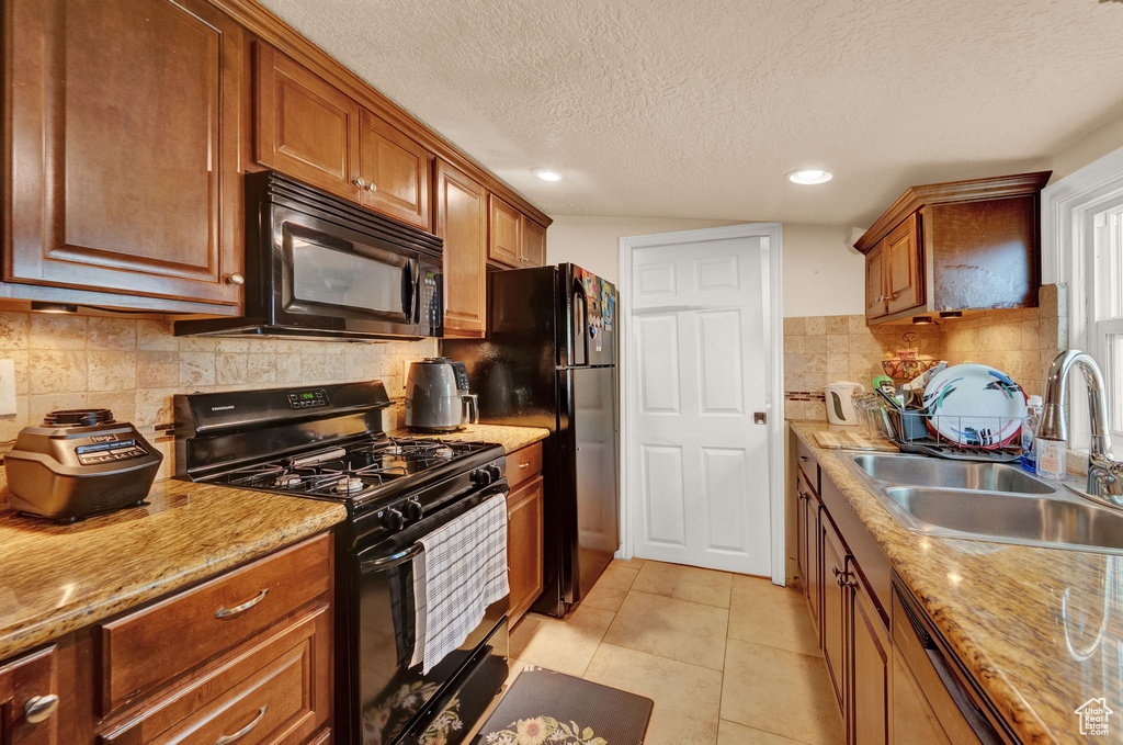 Kitchen featuring light tile floors, a textured ceiling, sink, backsplash, and black appliances