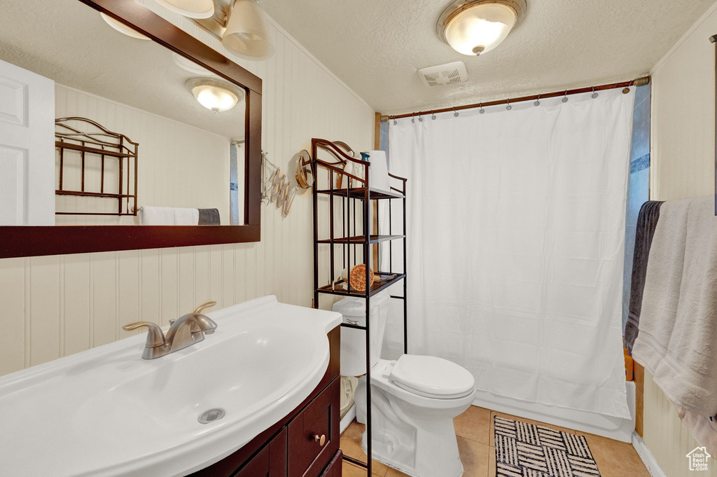 Bathroom with a textured ceiling, tile floors, vanity with extensive cabinet space, and toilet
