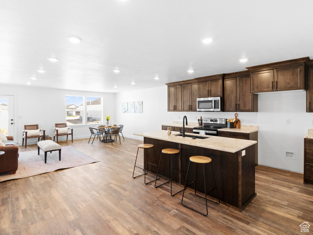 Kitchen with light stone counters, appliances with stainless steel finishes, sink, hardwood / wood-style floors, and an island with sink