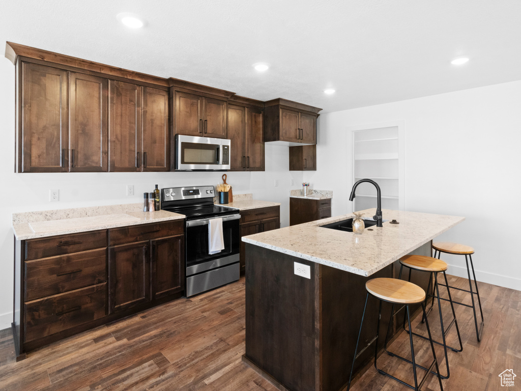Kitchen featuring sink, stainless steel appliances, a center island with sink, dark hardwood / wood-style floors, and dark brown cabinetry