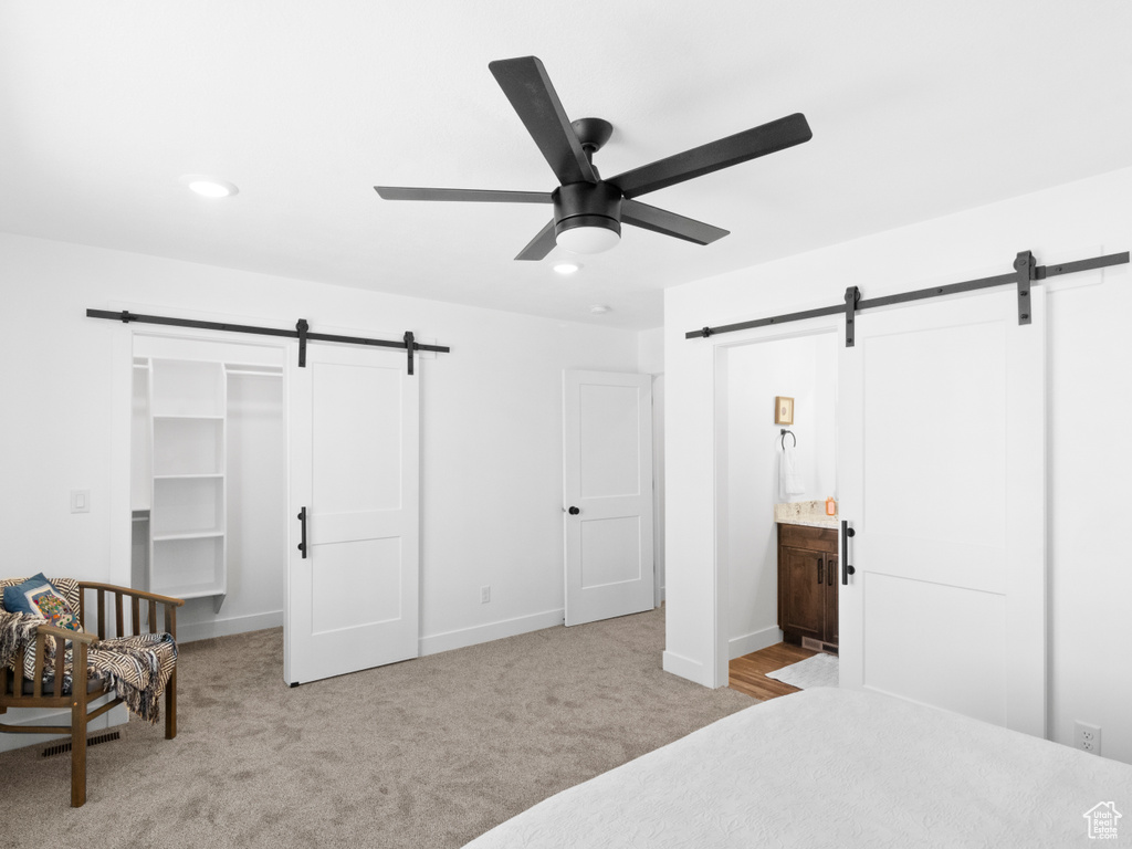 Carpeted bedroom featuring a closet, ceiling fan, ensuite bath, and a barn door